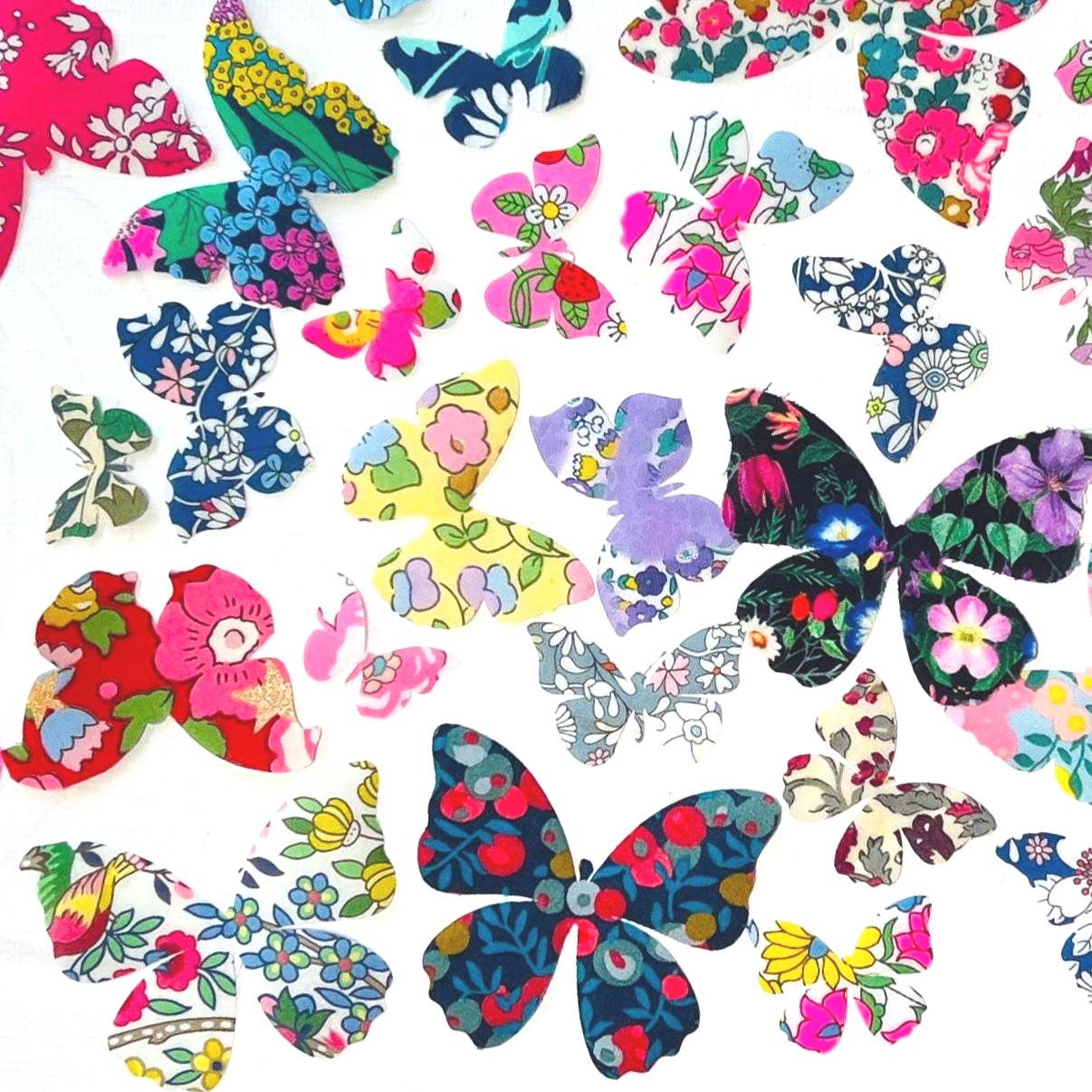 May include: A collection of fabric butterfly cutouts in various sizes and colors. The butterflies feature floral patterns in shades of pink, blue, yellow, and green. The cutouts are arranged on a white background.